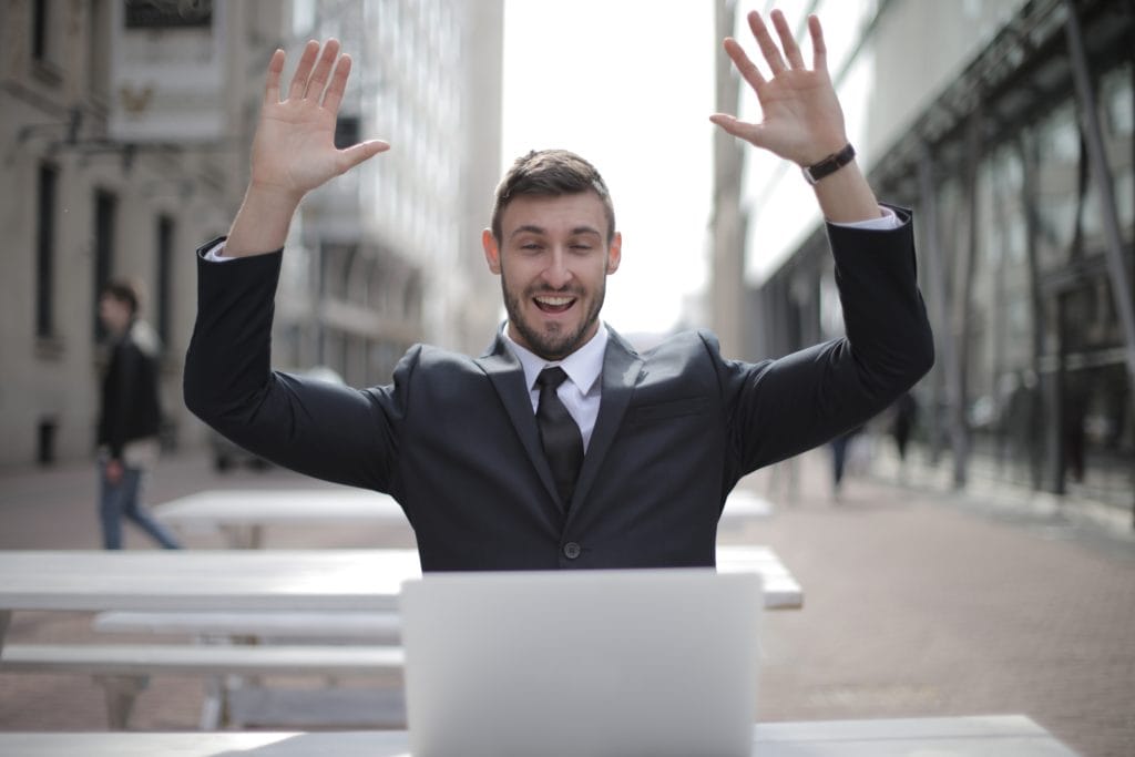 Man with suit celebrating while working on his laptop. 