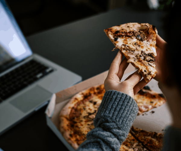 A person working in the laptop and eating pizza